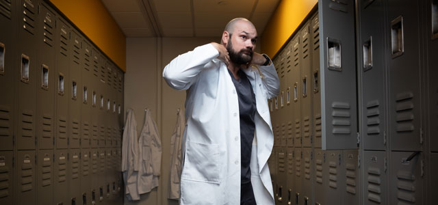 Resident putting on his lab coat in a locker room.