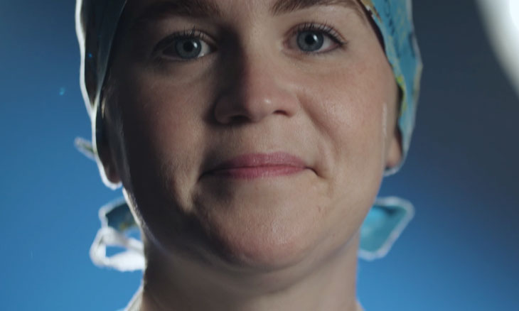 Nurse in surgical scrubs smiles at camera.